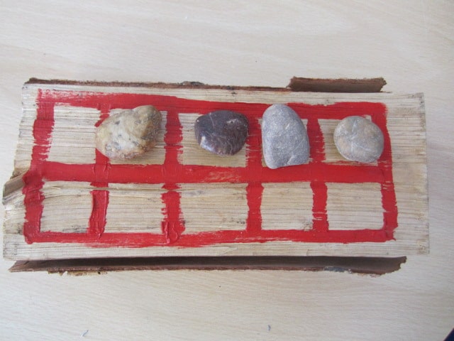 A wooden ten frame, with pebbles for counting