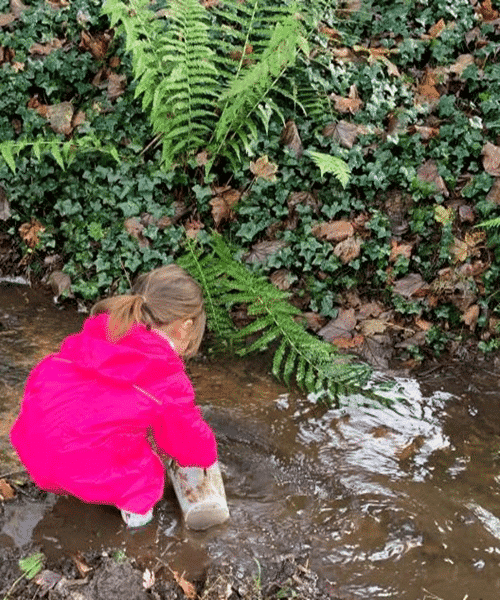 A girl scoops water from a puddle using a container from the mud kitchen