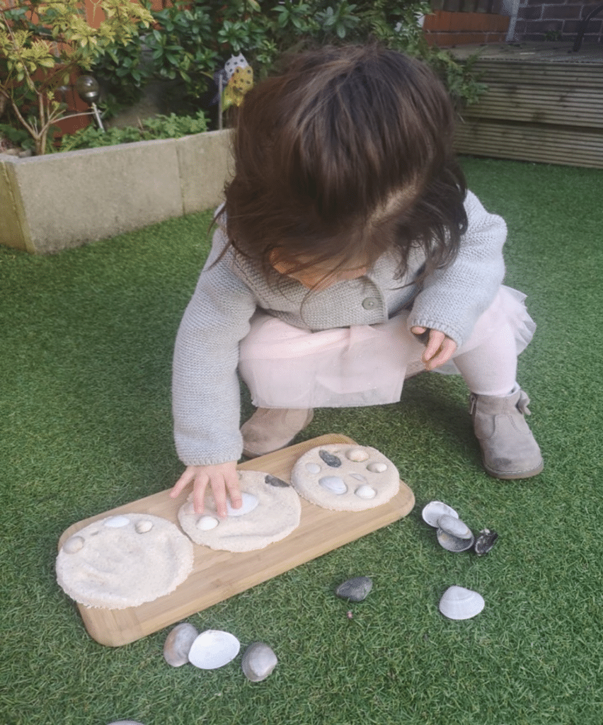 A girl using a positional schema to arrange shells on a clay plaque