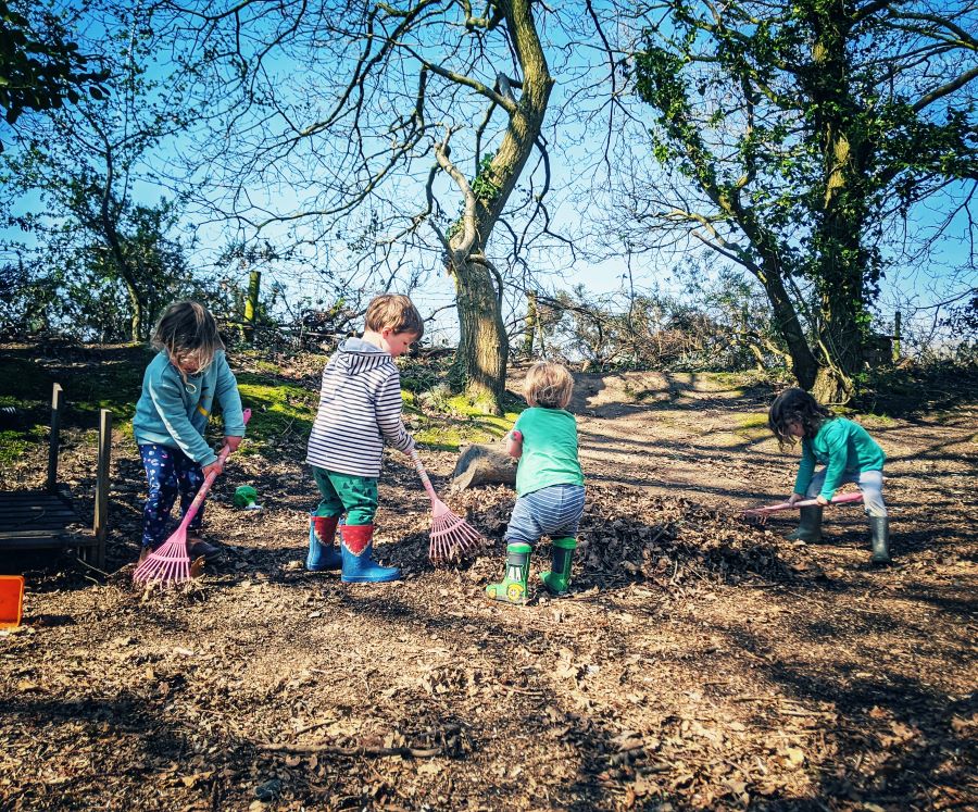 Group of children raking leaves in a forest school