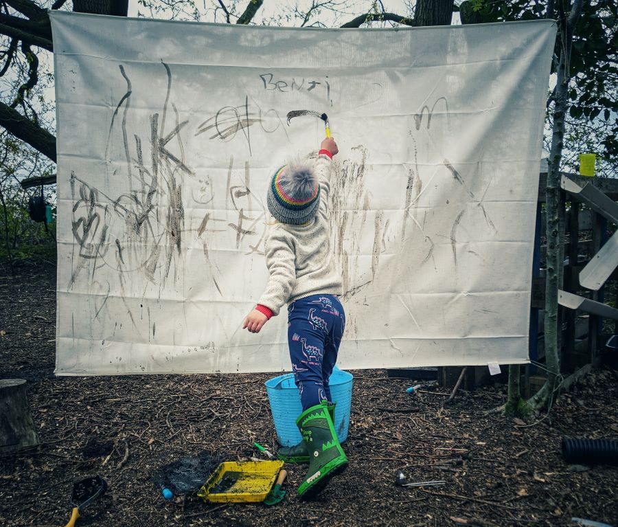 A child drawing with mud with a paintbrush in a forest school